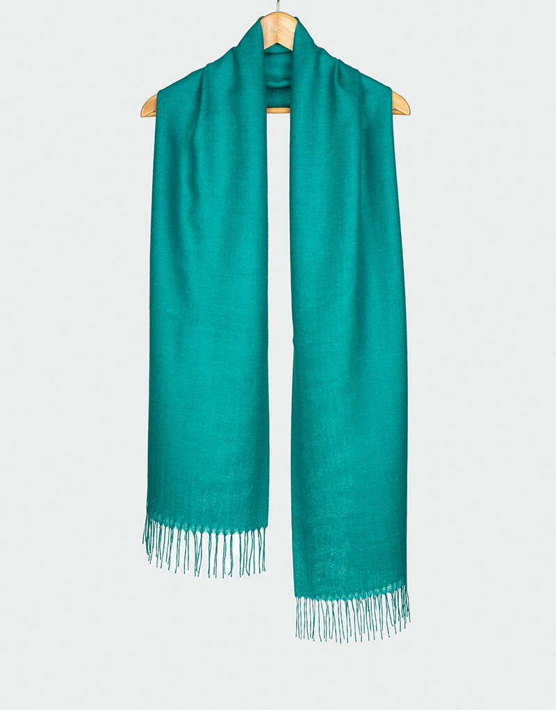 Bufanda verde turquesa con flecos claros diseño liso de textura suave colgada en gancho de madera
