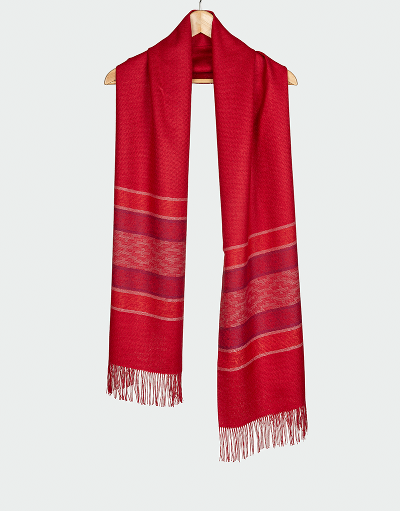 Bufanda roja con franjas horizontales en tonos rojo oscuro y beige con flecos finos diseño cálido artesanal colgada en gancho de madera