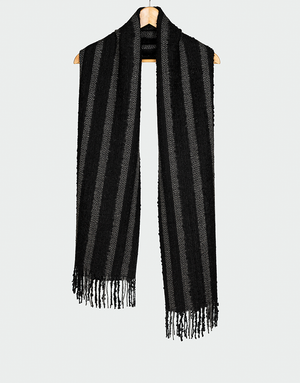 Bufanda negra con franjas verticales gris oscuro y textura suave con flecos finos estilo atemporal colgada en gancho de madera