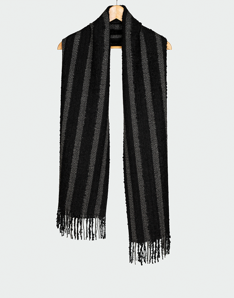 Bufanda negra con franjas verticales gris oscuro y textura suave con flecos finos estilo atemporal colgada en gancho de madera