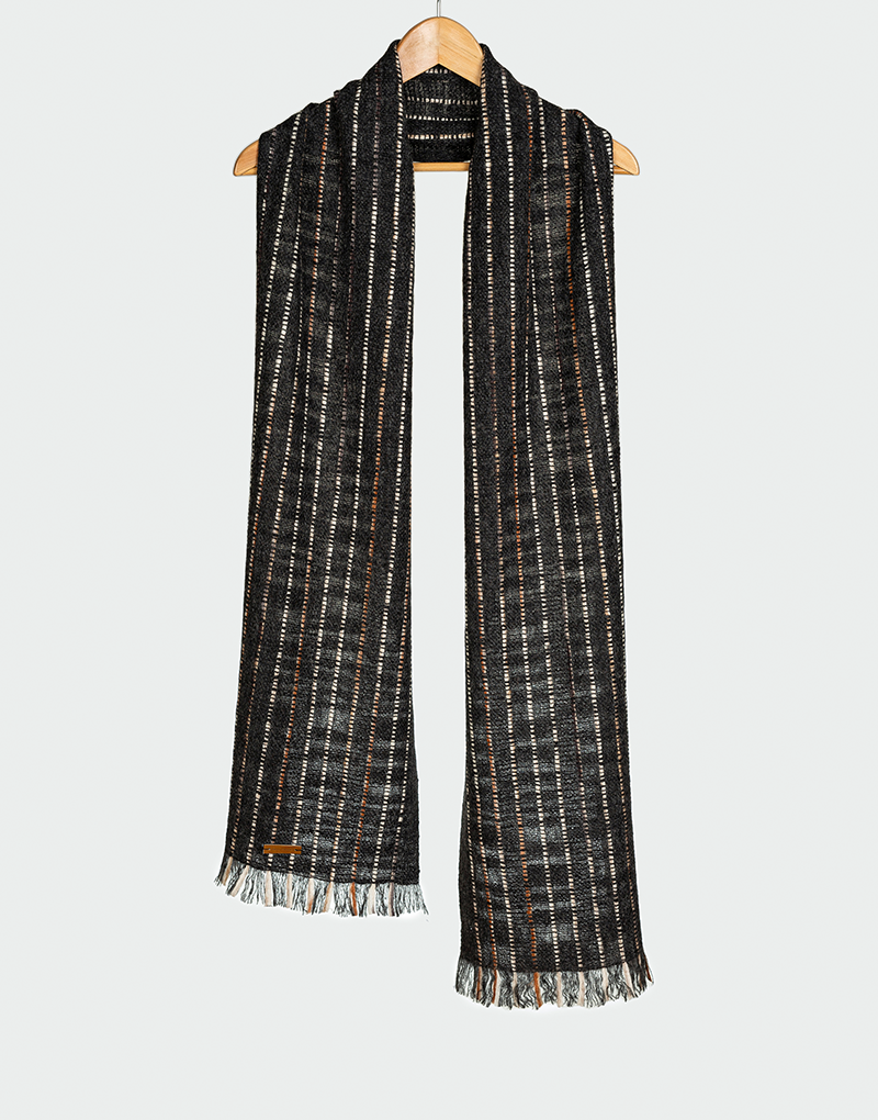 Bufanda tejida en patrón de rayas verticales en negro gris y marrón con textura ligera y flecos finos colgada en gancho de madera