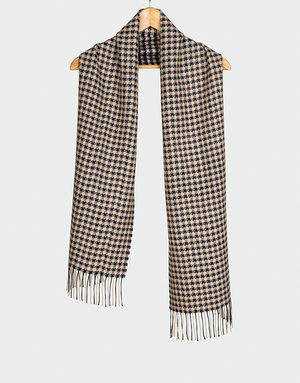 Bufanda con diseño pata de gallo en tonos beige y azul marino con flecos blancos colgada en gancho de madera