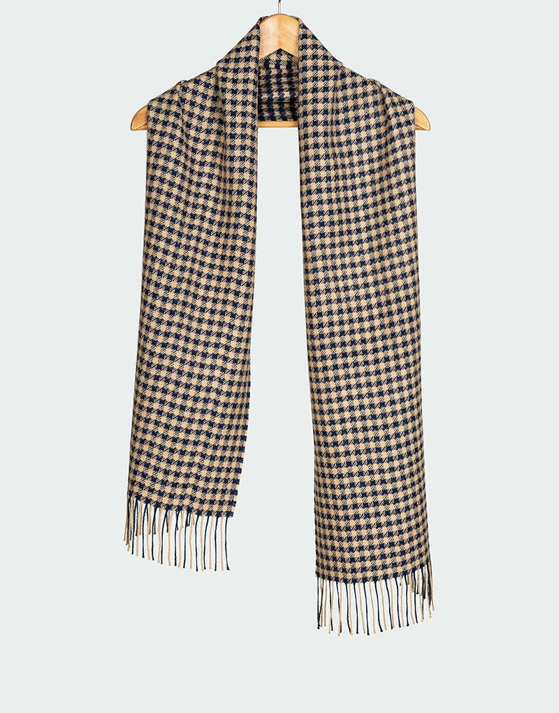 Bufanda con diseño pata de gallo en tonos beige y azul marino con flecos blancos colgada en gancho de madera