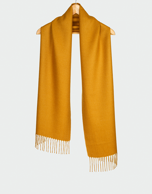 Bufanda color mostaza dorado con flecos colgada en gancho de madera ideal para acentos de color en invierno