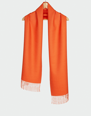Bufanda naranja terracota con flecos blancos colgada en gancho de madera ideal para looks cálidos y sofisticados
