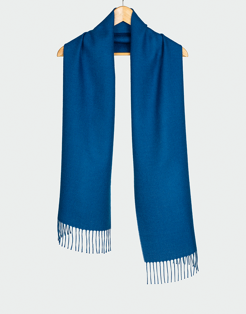 Bufanda azul rey con flecos blancos colgada en gancho de madera ideal para estilo invernal elegante
