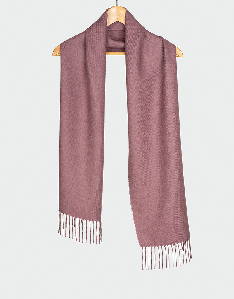 Bufanda color rosa malva suave con terminación en flecos colgada en gancho de madera estilo clásico y sofisticado