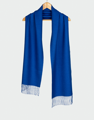 Bufanda azul cobalto con flecos finos colgada en gancho de madera ideal para moda de invierno elegante
