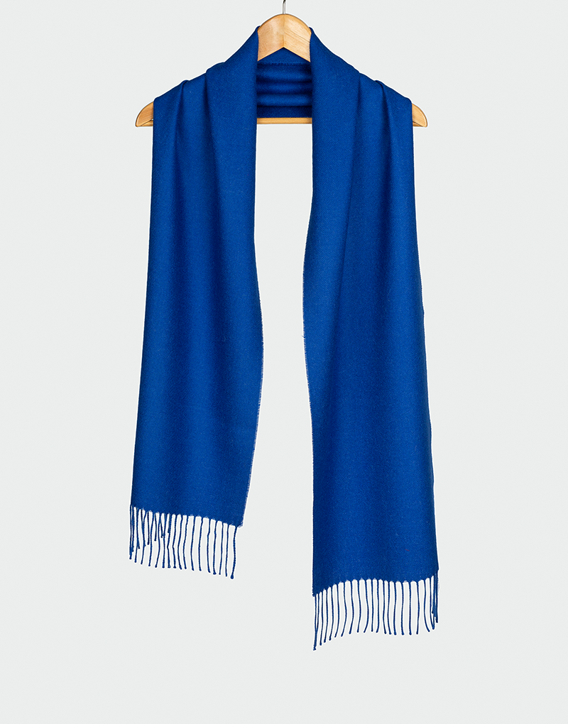 Bufanda azul cobalto con flecos finos colgada en gancho de madera ideal para moda de invierno elegante