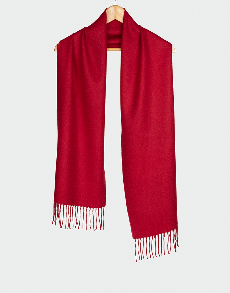 Bufanda rojo intenso con flecos decorativos colgada en gancho de madera perfecta para outfits de invierno llamativos