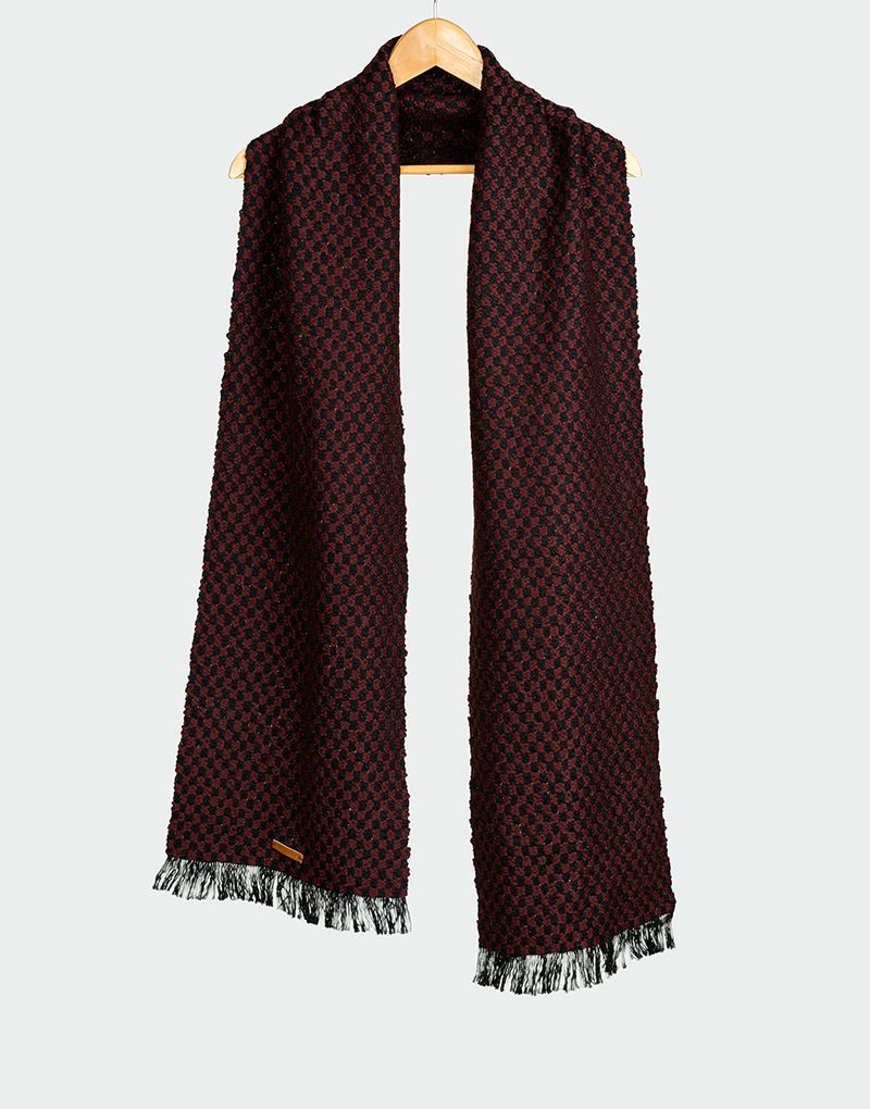 Chalina con patrón geométrico en rojo granate y negro con textura tejida y flecos en contraste colgada en gancho de madera estilo elegante