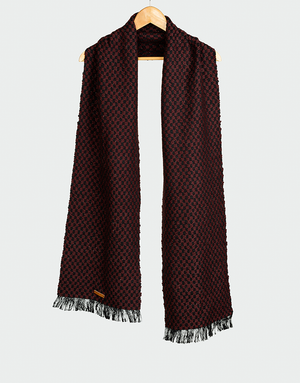 Chalina con patrón geométrico en rojo granate y negro con textura tejida y flecos en contraste colgada en gancho de madera estilo elegante