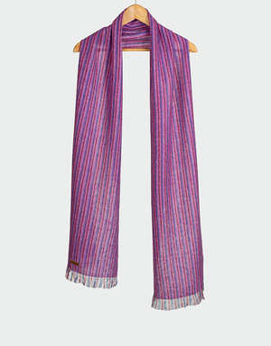 Chalina con rayas verticales en tonos púrpura fucsia y azul con flecos cortos colgada en gancho de madera diseño vibrante artesanal