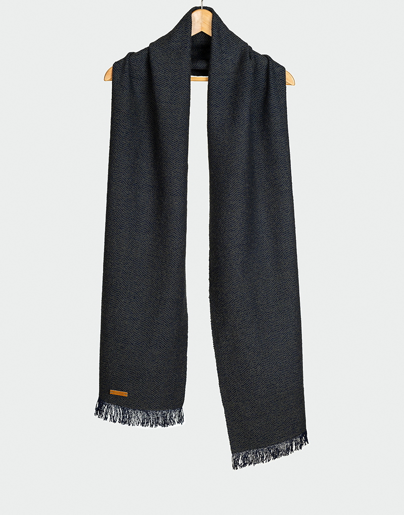 Chalina azul marino con diseño de espiguilla en contraste sutil y terminación en flecos cortos estilo clásico colgada en gancho de madera