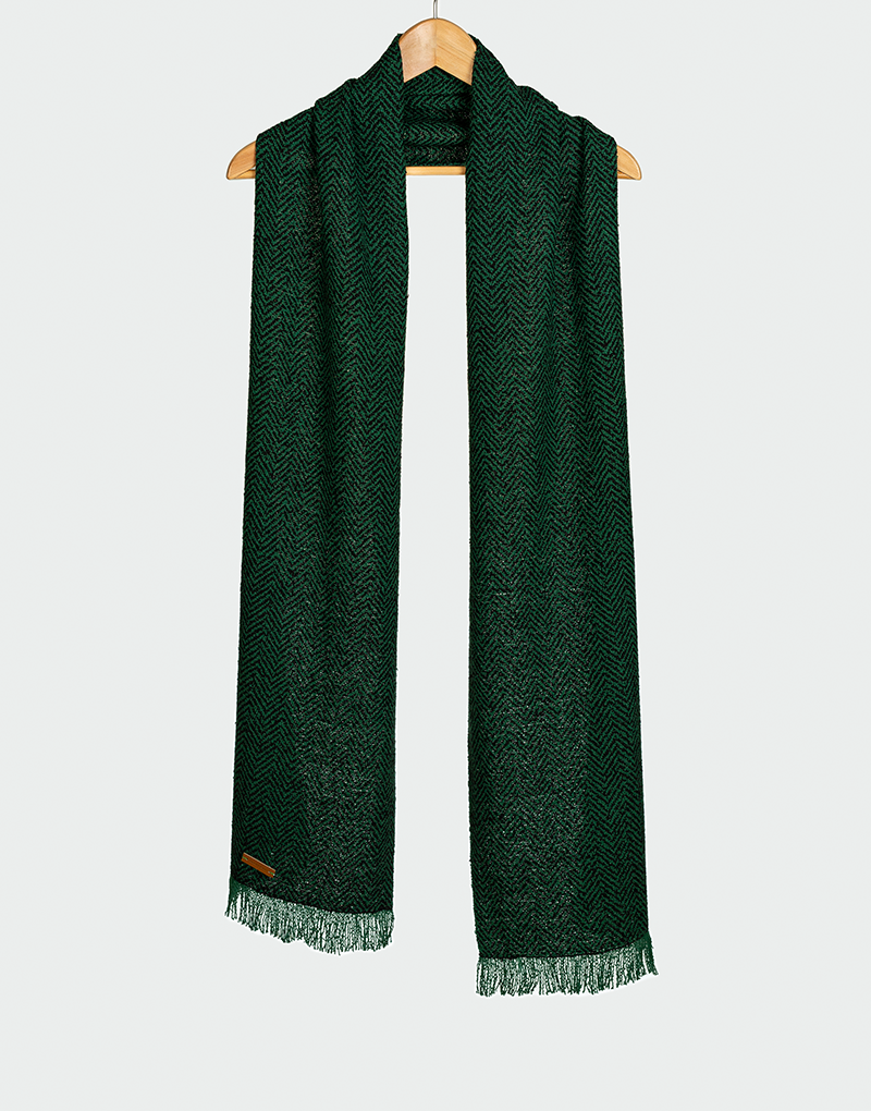 Chalina verde oscuro con patrón de espiguilla y flecos cortos colgada en gancho de madera diseño elegante y texturizado